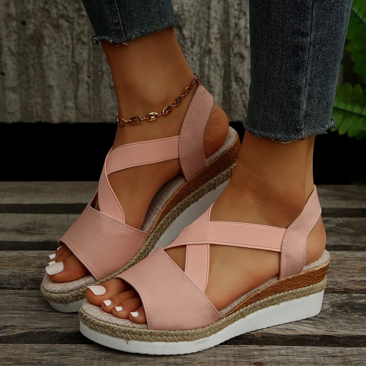 Pink wedge sandals with a wooden sole worn by a person on a wooden floor.