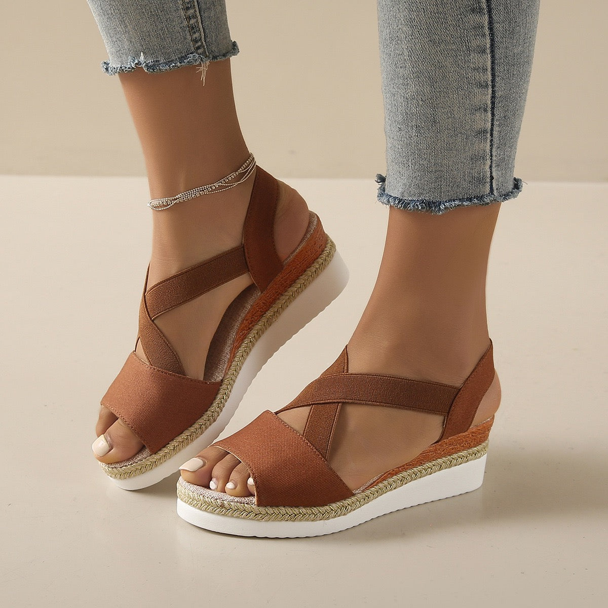 Brown wedge sandals worn with light blue jeans on a beige background