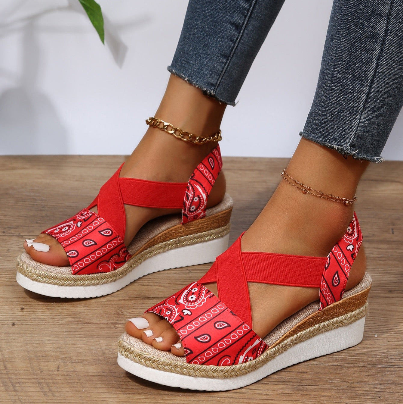 Red patterned sandals worn with jeans on a wooden floor.