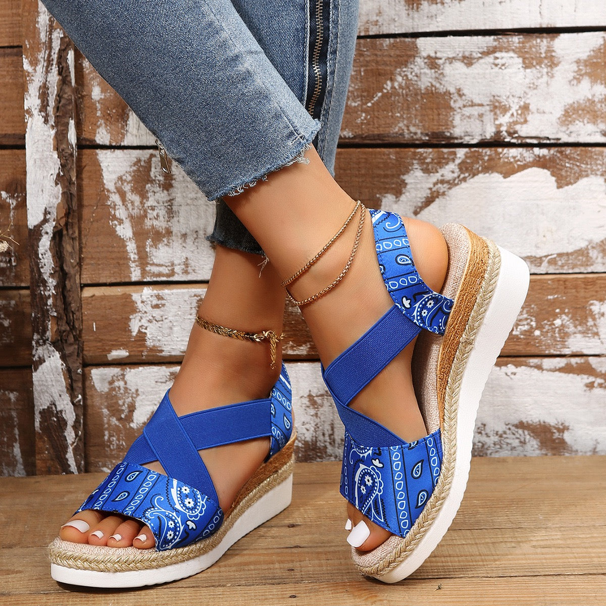 Blue bandana-patterned sandals on a wooden floor with denim jeans.